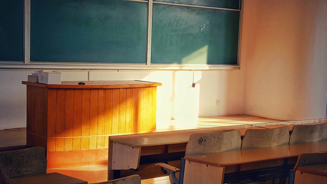 An empty classroom with rows of desks and a chalkboard